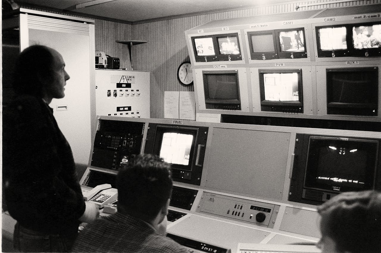 Men working in a vintage broadcasting control room filled with analogue equipment and monitors.